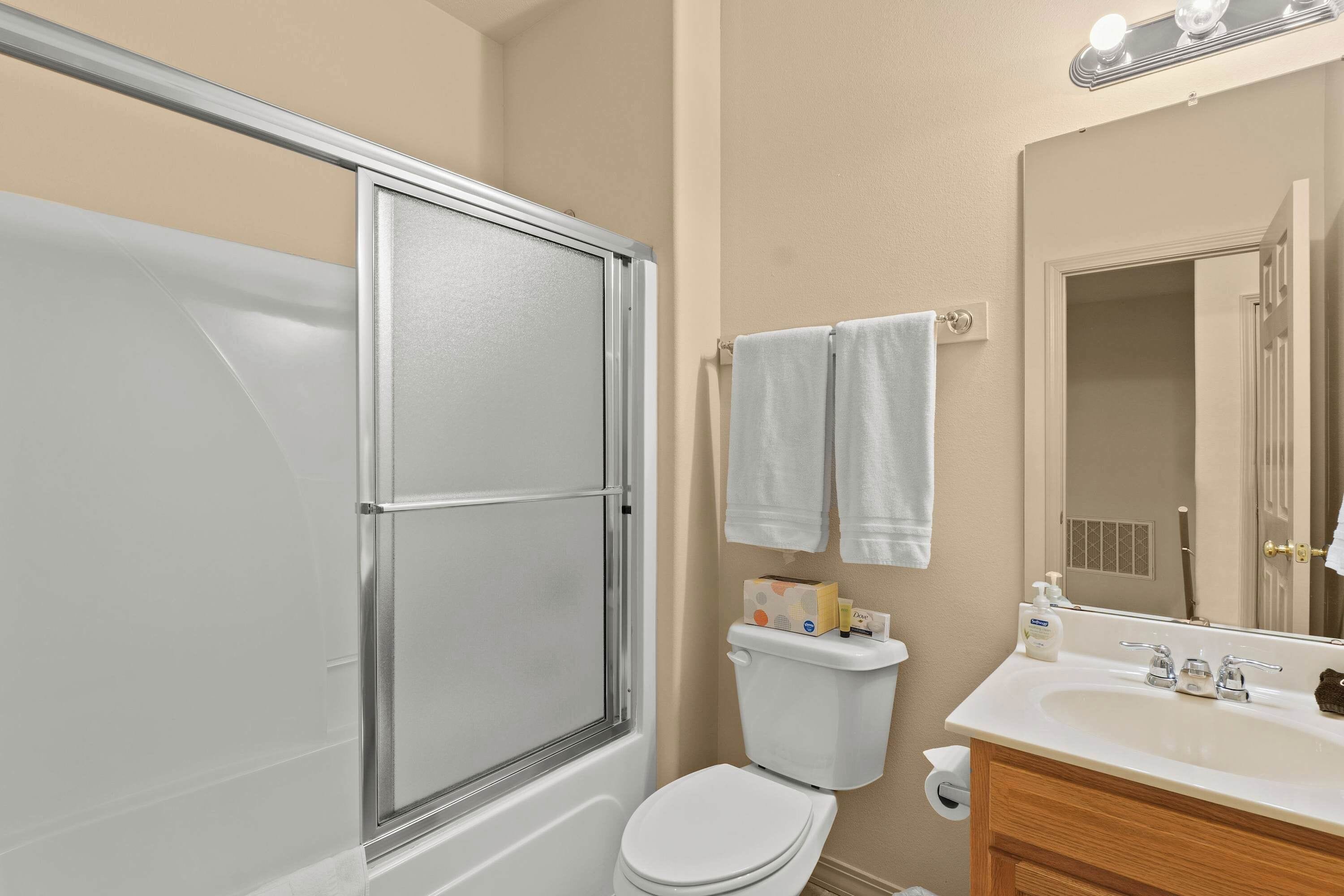 Un baño con ducha envuelta en vidrio, un inodoro, un lavabo con tocador y un espejo.