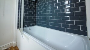 Un baño con una bañera blanca, paredes de azulejos negros y una ducha.