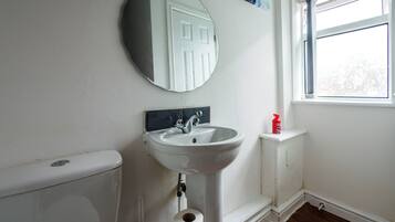Ein Badezimmer mit einem weißen Waschbecken, einem runden Spiegel, einer Toilette und einem Fenster.
