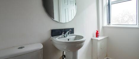 Un baño con un lavamanos blanco, un espejo redondo, un inodoro y una ventana.