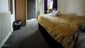 Habitación de hotel con cama, radiador, armario de madera, cubo de basura y ventana con cortinas.