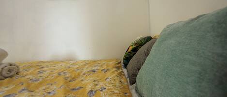 A bed with a floral bedspread, a green blanket, and a pillow with a leaf pattern.