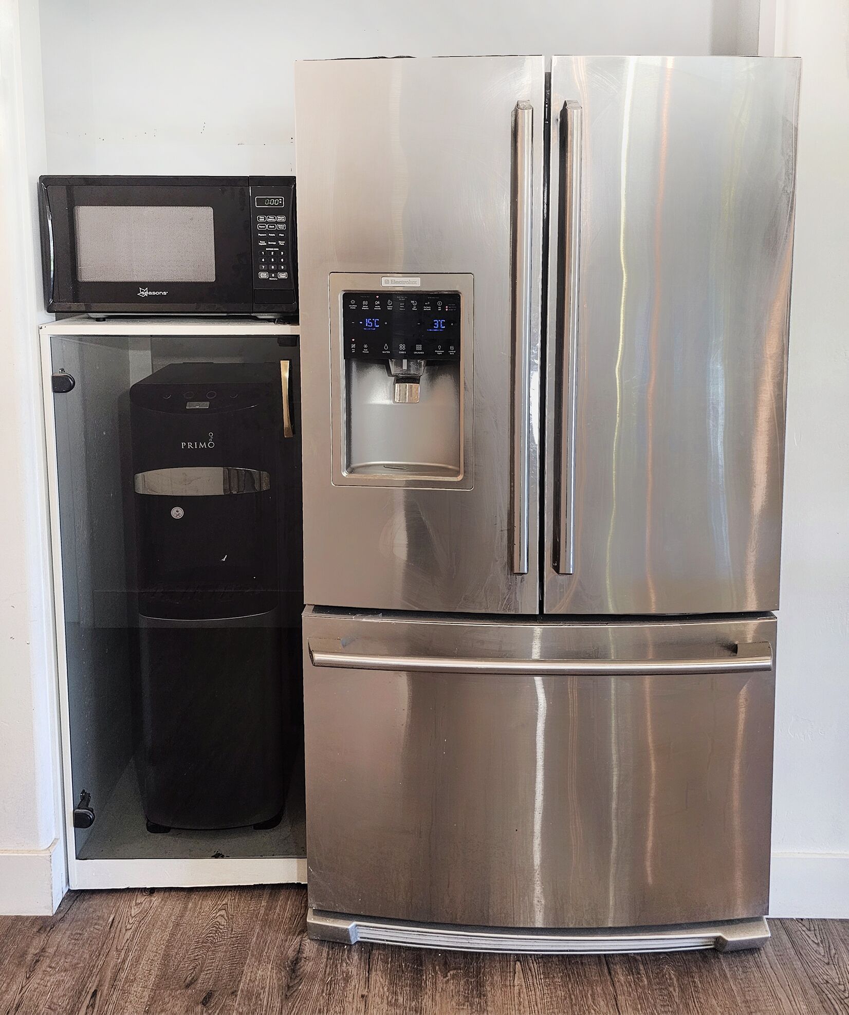 A stainless steel refrigerator with a water dispenser and a microwave above it.