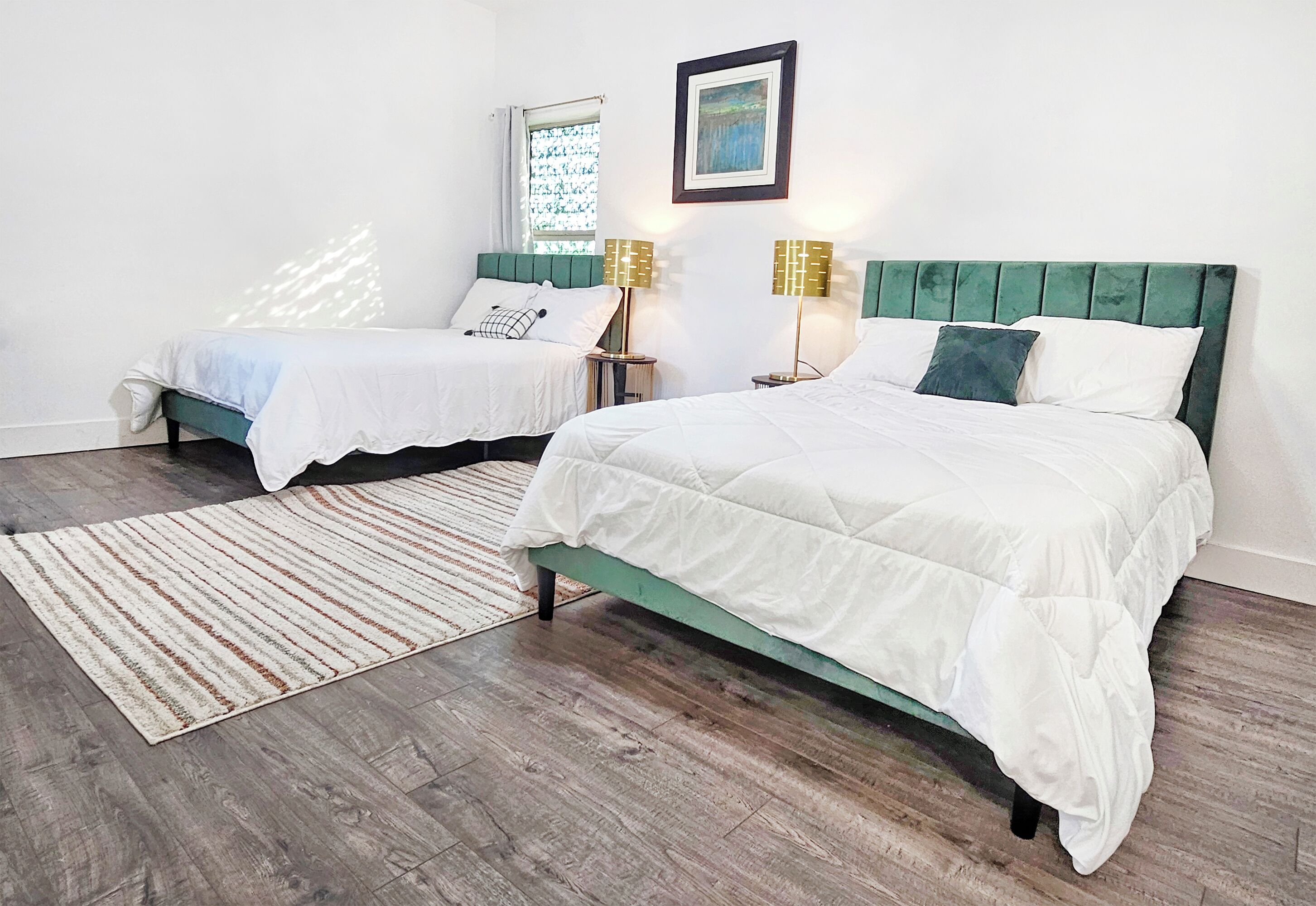 A bedroom with two beds, a wooden floor, a striped rug, and a window with a view.