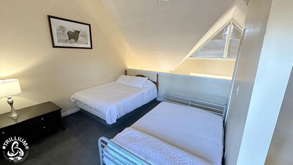 A room with two beds, a bedside table with a lamp, and a framed picture on the wall.