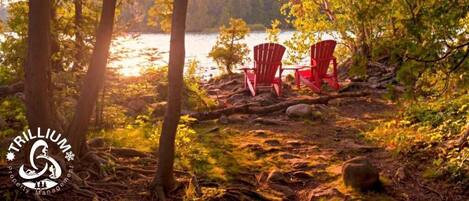 Un entorno tranquilo junto al lago con sillas Adirondack rojas y el logotipo de Trillium Property Management a la vista.