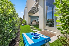 A modern building with a glass entrance, a patio area with a blue table, and a pathway leading to the entrance.