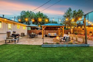 A backyard patio with a covered seating area, a barbecue setup, and string lights.