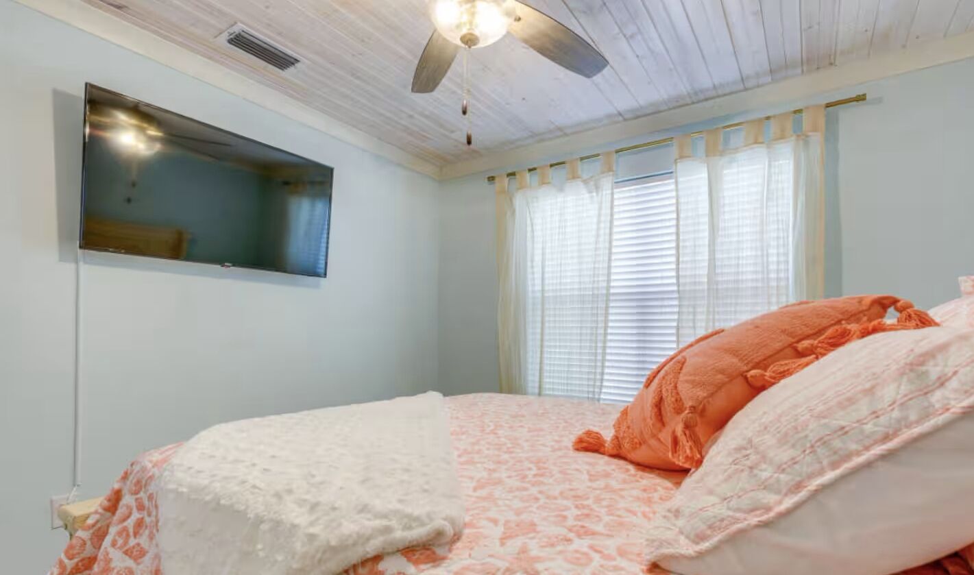 Un dormitorio con una cama, ventilador de techo, ventana con persianas y estante fijado a la pared.