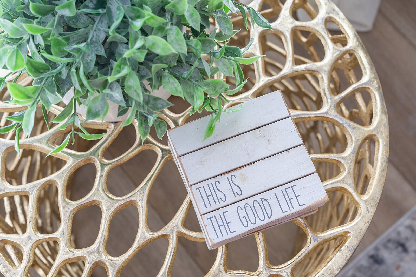 Een decoratief bord met de tekst 'THIS IS THE GOOD LIFE' op een rustieke houten ondergrond.