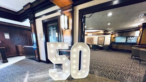 Eine Hotelhalle mit einer großen, beleuchteten '50' Beschilderung, einem Empfangstresen und einem gemusterten Teppich.
