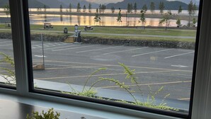 Vista desde una ventana sobre un estacionamiento con un lago y montañas al fondo.