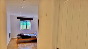 A narrow hallway leading to a bedroom with a bed, a window, and a radiator.