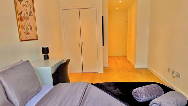 A bedroom with a bed, a desk, a chair, a wardrobe, and a framed botanical print on the wall.