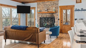 Una sala de estar con chimenea de piedra, televisor, sofá de cuero marrón y sillón azul.