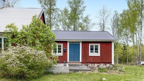 Una casa de madera roja con puerta azul, ventanas blancas y cimientos de piedra.