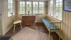 Una habitación acogedora con un banco de madera, una mesa de madera y vistas a la vegetación a través de amplios ventanales.