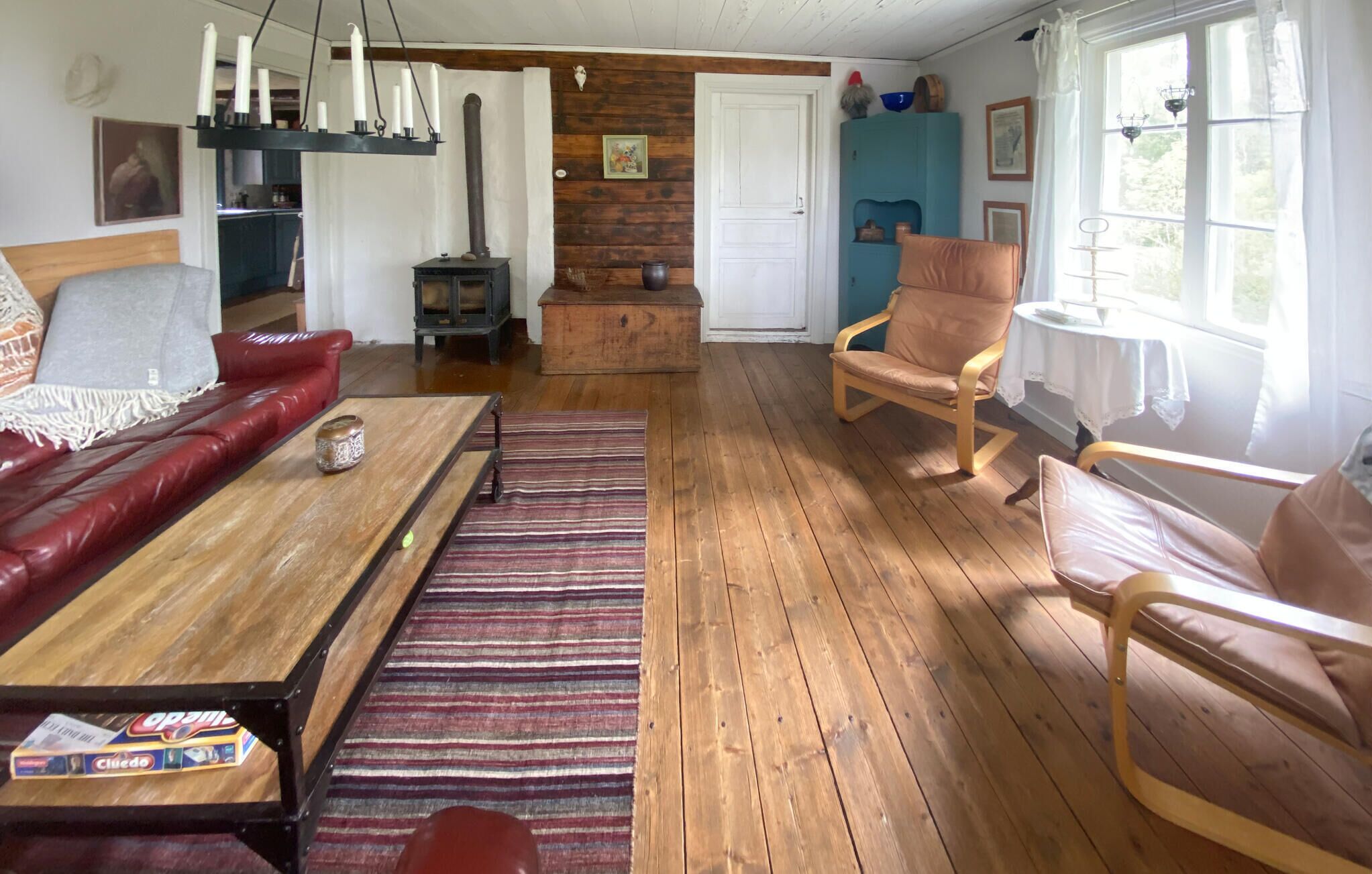 A cozy living room with a red leather sofa, a wooden coffee table, and a striped rug. There is a blue cabinet with decorative items and a wooden stove in the background.
