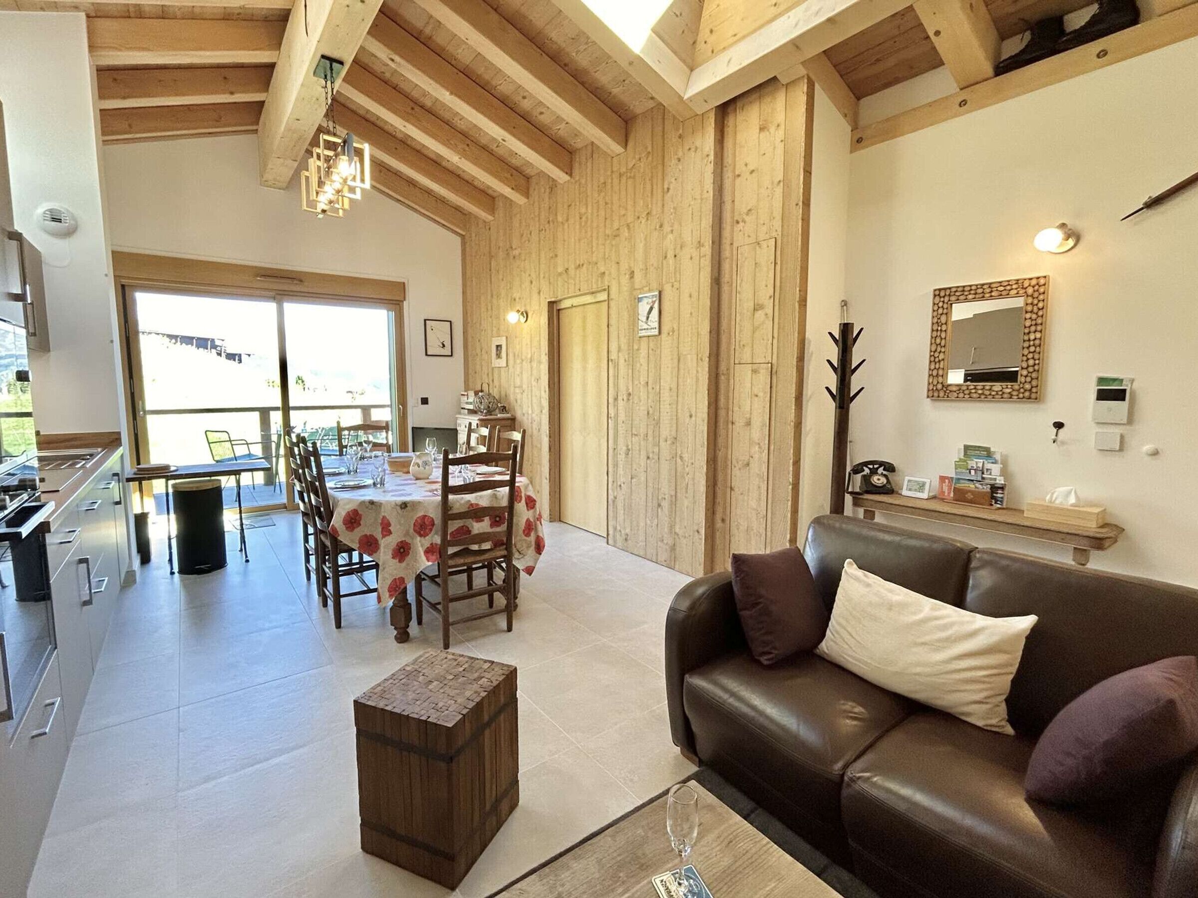 A spacious living area with a wooden ceiling, a dining table set for four, and a leather sofa.