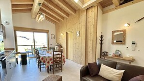 Ein geräumiger Wohnbereich mit Holzbalkendecke, einem für vier Personen gedeckten Esstisch und einem Ledersofa.