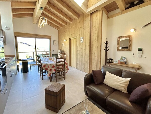 A spacious living area with a wooden ceiling, a dining table set for four, and a leather sofa. - 3-Room Apartment, Sleeps 4-6, Mountain View, Private Parking (Combloux)
