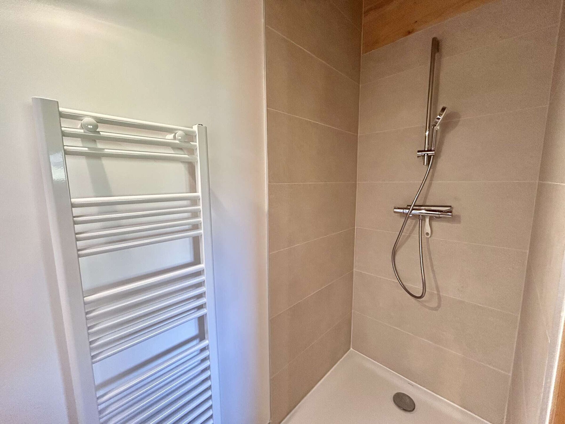 Een douche met een handdouche en een kraan op de muur, een witte handdoekhouder en een klein, leeg bad.