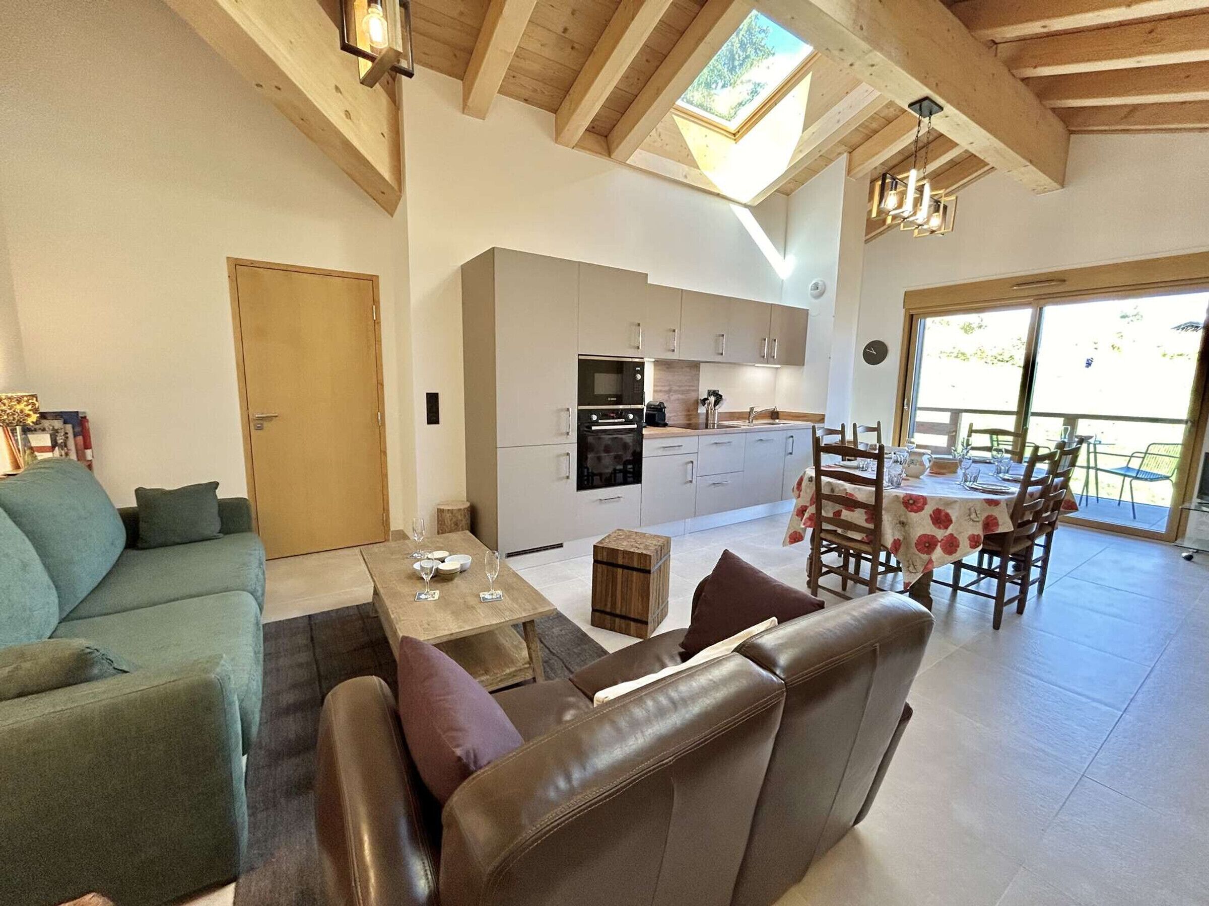 A spacious living area with a sofa, a coffee table, and a dining table set for four. A kitchen with modern appliances is visible in the background.