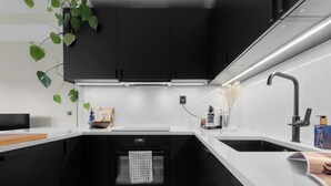 Een moderne keuken met zwarte kasten, witte aanrechtbladen en een ingebouwde oven.