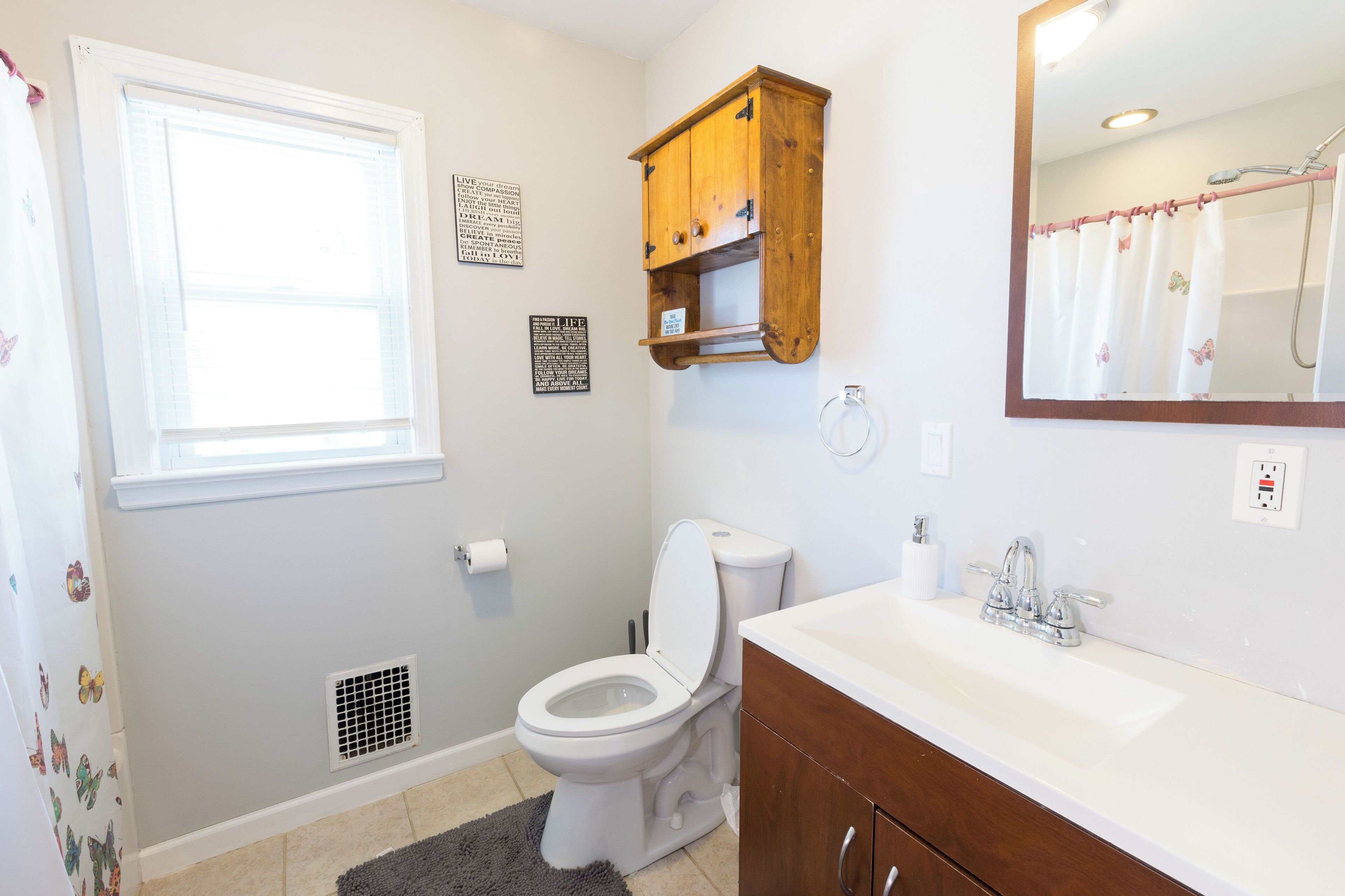 A bathroom with a toilet, sink, vanity, and a window.