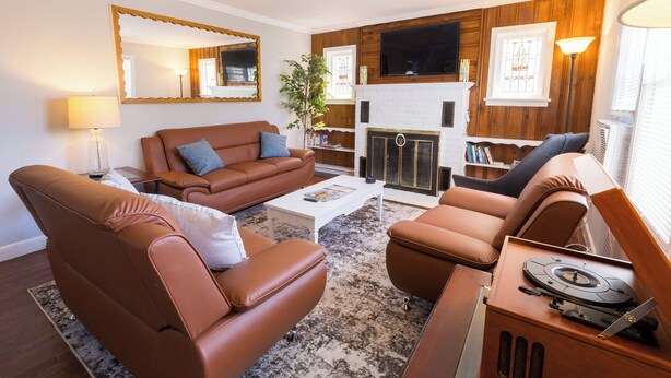 Ein Wohnzimmer mit Ledersofas, einem weißen Couchtisch, einem Kamin, einem Fernseher und einem Plattenspieler.