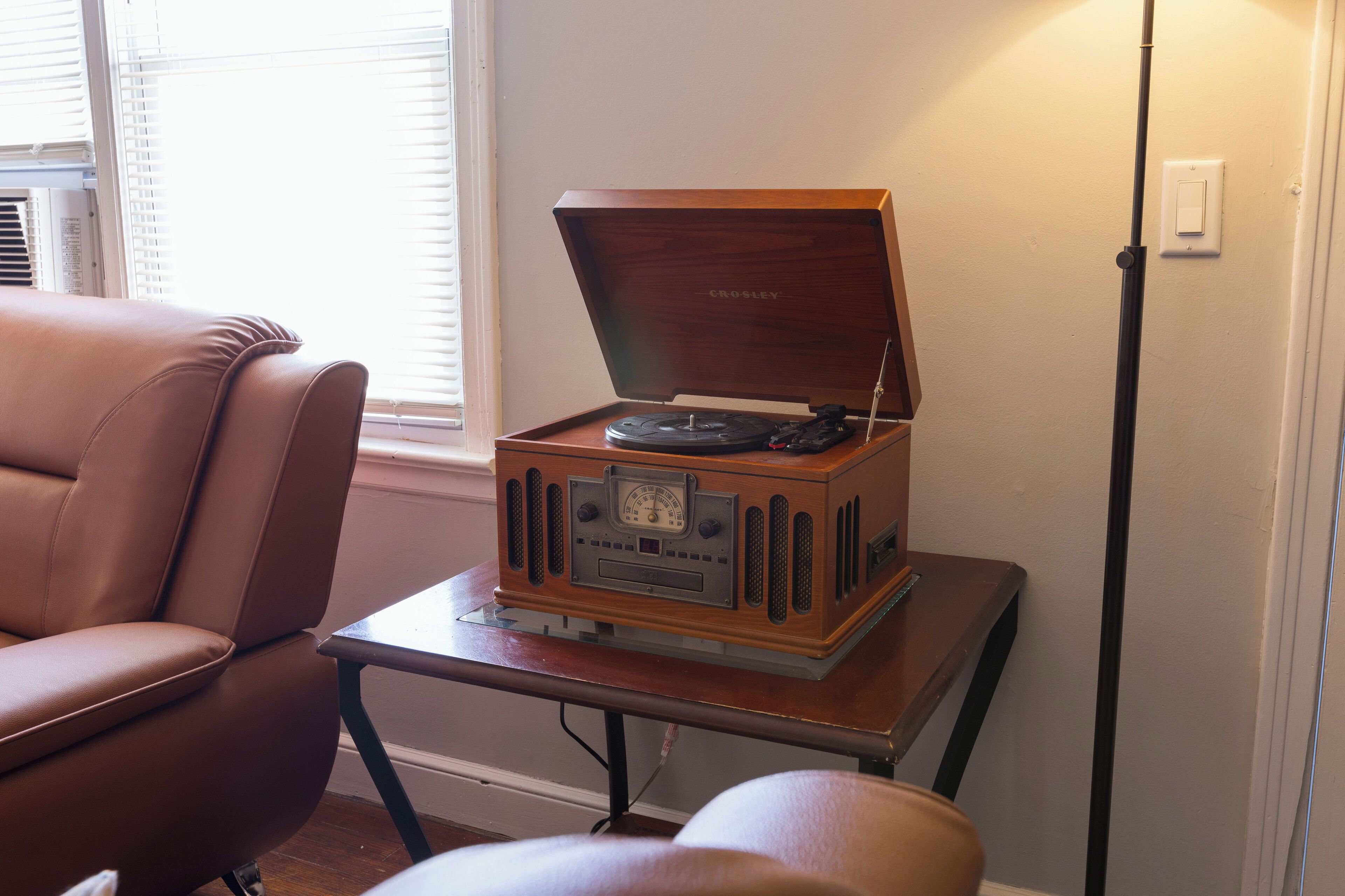 Een oude Crosley radio op een houten tafel in een kamer met een bruine leren stoel en een vloerlamp.