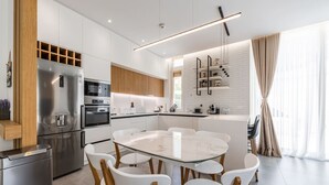 Une cuisine moderne dotée d’un îlot central, d’appareils électroménagers en acier inoxydable et d’un coin repas avec des chaises blanches et une table en verre.