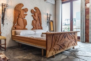Una cama con cabecera y piecera de madera tallada, suelo de piedra y vistas a través de una puerta de cristal.