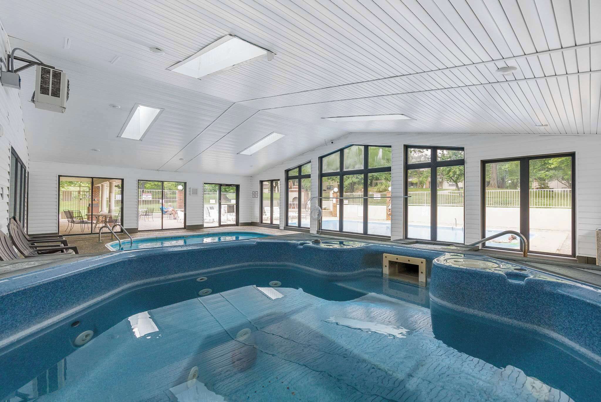 Una piscina interior con paredes de vidrio transparente, techo de madera y vistas al exterior.