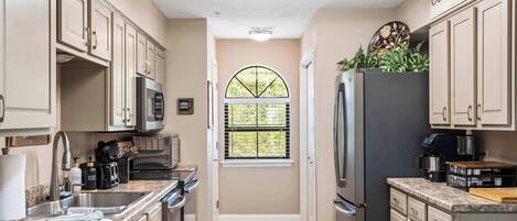 A kitchen with a built-in microwave, refrigerator, and sink. There is a window with a view of greenery outside.