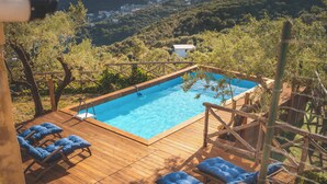 Una terraza de madera con piscina, sillas de descanso y vistas a zona boscosa.