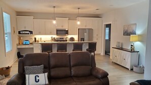 A modern living room with a brown leather sofa, a kitchen with white cabinets, a microwave, and a refrigerator. - Charming 3-bedroom home within walking distance to  downtown area/FLETC friendly (Darien)