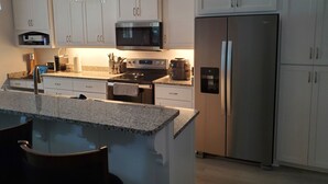 A modern kitchen with white cabinets, stainless steel appliances, granite countertops, and a central island with seating. - Charming 3-bedroom home within walking distance to  downtown area/FLETC friendly (Darien)