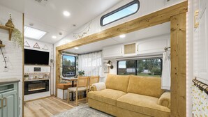 A cozy RV interior with a sofa, a dining area, a TV, and a kitchen. - Tiny Home Near Tetons & Island Park! (Felt)