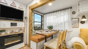 A cozy RV interior with a TV, fireplace, dining table, and comfortable seating. - Tiny Home Near Tetons & Island Park! (Felt)