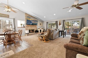 A spacious living room with a fireplace, a dining area with wooden chairs, a sofa, and a ceiling fan. - Gutierrez Getaway (Big Bear City)