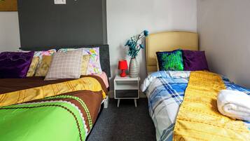 A hotel room with two beds, a nightstand, and a wall-mounted TV.