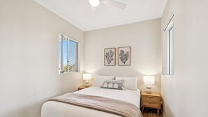 A bedroom with a bed, two bedside tables, a ceiling fan, and two windows. - Sunray – Beachside Bliss Sawtell, Beach, Village (Sawtell)