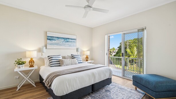 A bedroom with a bed, bedside tables, a ceiling fan, a large window with a view, and a balcony. - Sunray – Beachside Bliss Sawtell, Beach, Village (Sawtell)