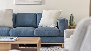 A blue sofa with white cushions, a wooden coffee table, a small plant, and a framed abstract painting on the wall. - Sunray – Beachside Bliss Sawtell, Beach, Village (Sawtell)