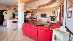 Een ruime woonkamer met een rode bank, een eettafel en een keuken op de achtergrond.
