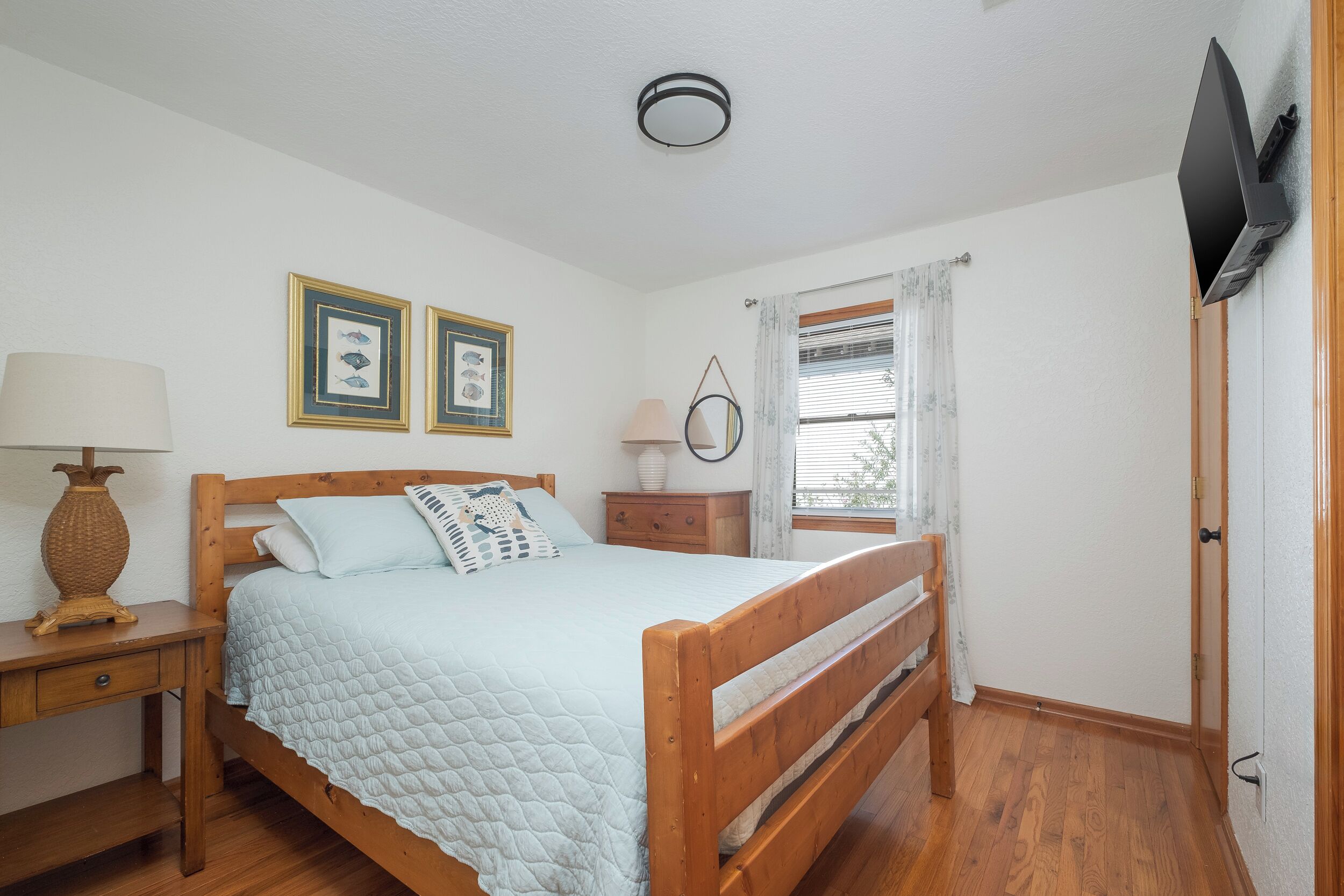 Un dormitorio con una cama de madera, una mesita de noche con lámpara, un aparador y una ventana con cortinas.