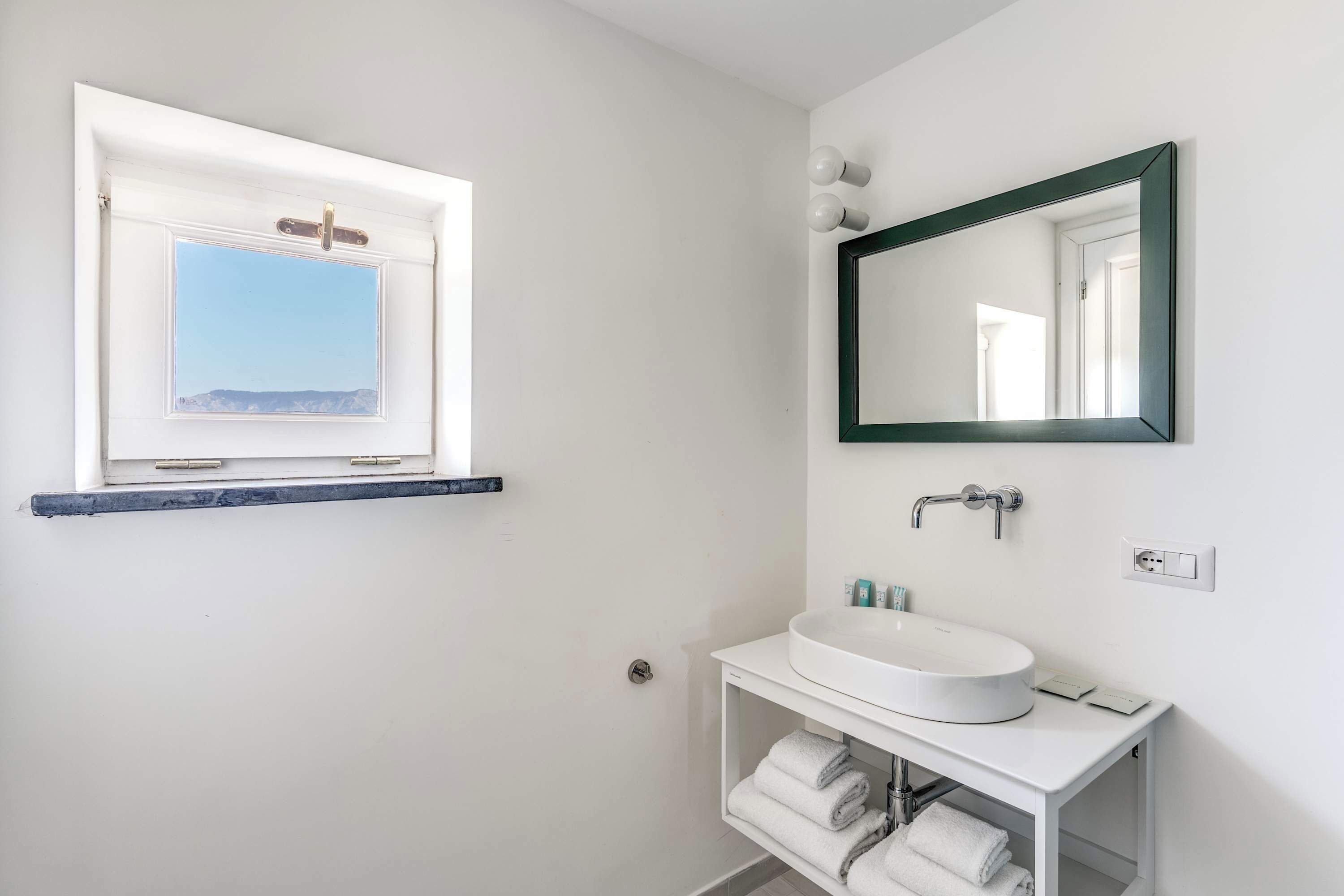 A bathroom with a white sink, a mirror, a window with a view, and a towel rack.