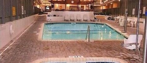 An indoor swimming pool area with two pools, lounge chairs, and a brick floor.