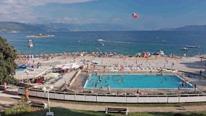Un espace piscine au bord de la plage, comprenant plusieurs piscines, des parasols et des personnes se baignant ou se relaxant sur la plage.